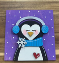 Hand-painted penguin frame insert with blue earmuffs and scarf, white snowflake, red heart, and purple snowy background.