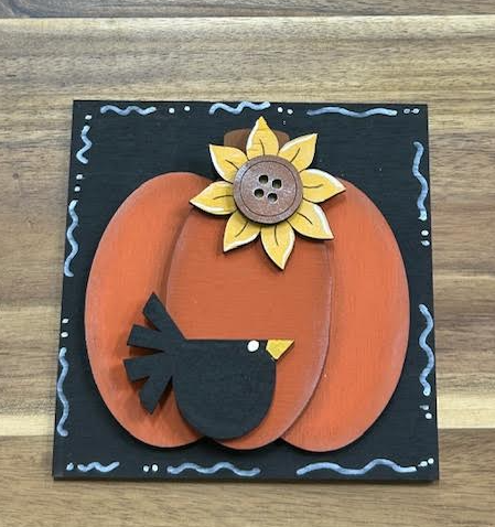 Finished orange pumpkin frame insert with black bird and yellow flower on a decorated black background