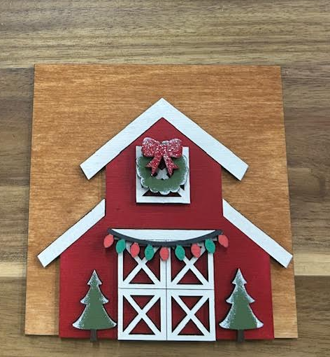 Hand-painted red Christmas barn frame insert with white trim, green wreath and red bow, holiday lights, and two evergreen trees on a warm wood-toned background.