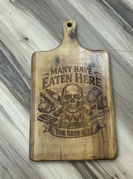 Large paddle acacia charcuterie board engraved with Many Have Eaten Here, Few Have Died design