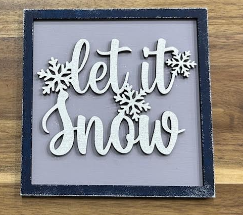Hand-painted Let It Snow frame insert with white lettering and snowflakes on a gray background, shown in a dark frame