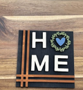 Finished HOME frame insert with white letters on black, green wreath, blue heart, and brown line accents.