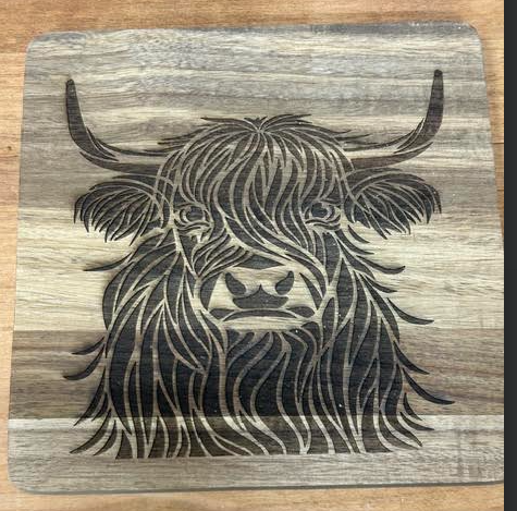 Square 8 x 8 inch acacia wood trivet with a detailed engraved Highland cow design