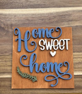 Finished Home Sweet Home frame insert with blue and white lettering, a white heart, and green leafy accent on a warm brown background.