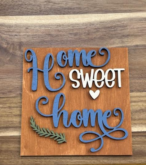 Finished Home Sweet Home frame insert with blue and white lettering, a white heart, and green leafy accent on a warm brown background.
