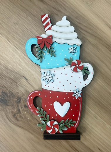 Hand-painted stacked hot cocoa mugs shelf sitter with turquoise, white, and red mugs, peppermint accents, greenery, and whipped cream.