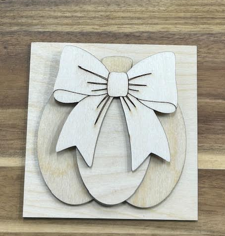 Unfinished wood pumpkin with a large layered bow on a square frame insert